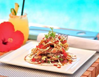 a square plate of food served poolside with a tropical drink