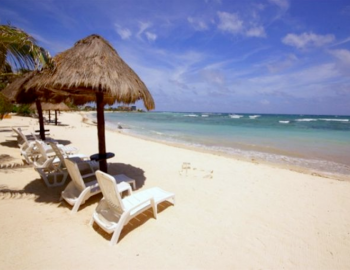 a pair of beach chairs underneath thatched umbrellas face the pacific ocean