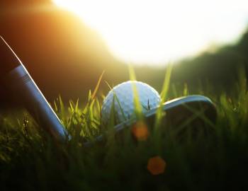the head of a 60-degree wedge lined up with a golf ball in the rough