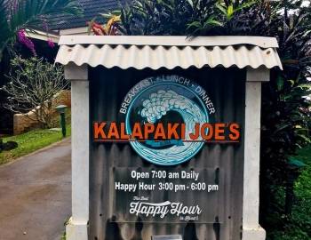 a sign with "kalapaki joe's" written in orange in front of a graphic of a cresting wave