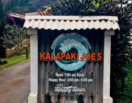 a sign with "kalapaki joe's" written in orange in front of a graphic of a cresting wave